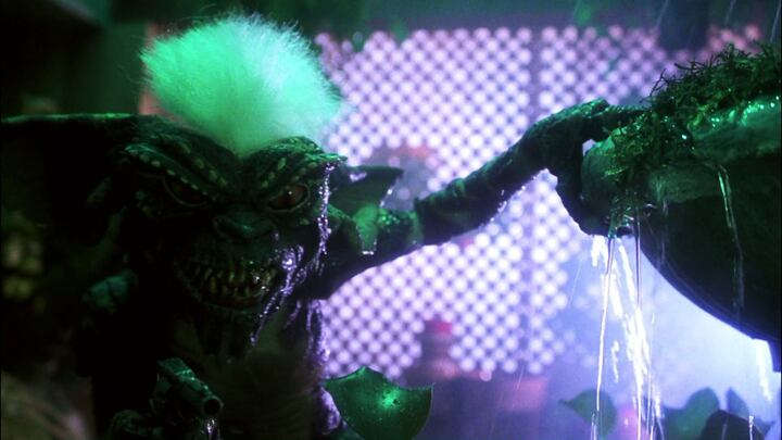 Fotograma de la cinta 'Gremlins' de 1984, mostrando a Stripe agarrado de una fuente y apuntando con un arma.